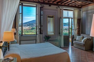 Una camera da letto con un letto grande, un angolo salotto con divano e un balcone con vista sulla campagna.