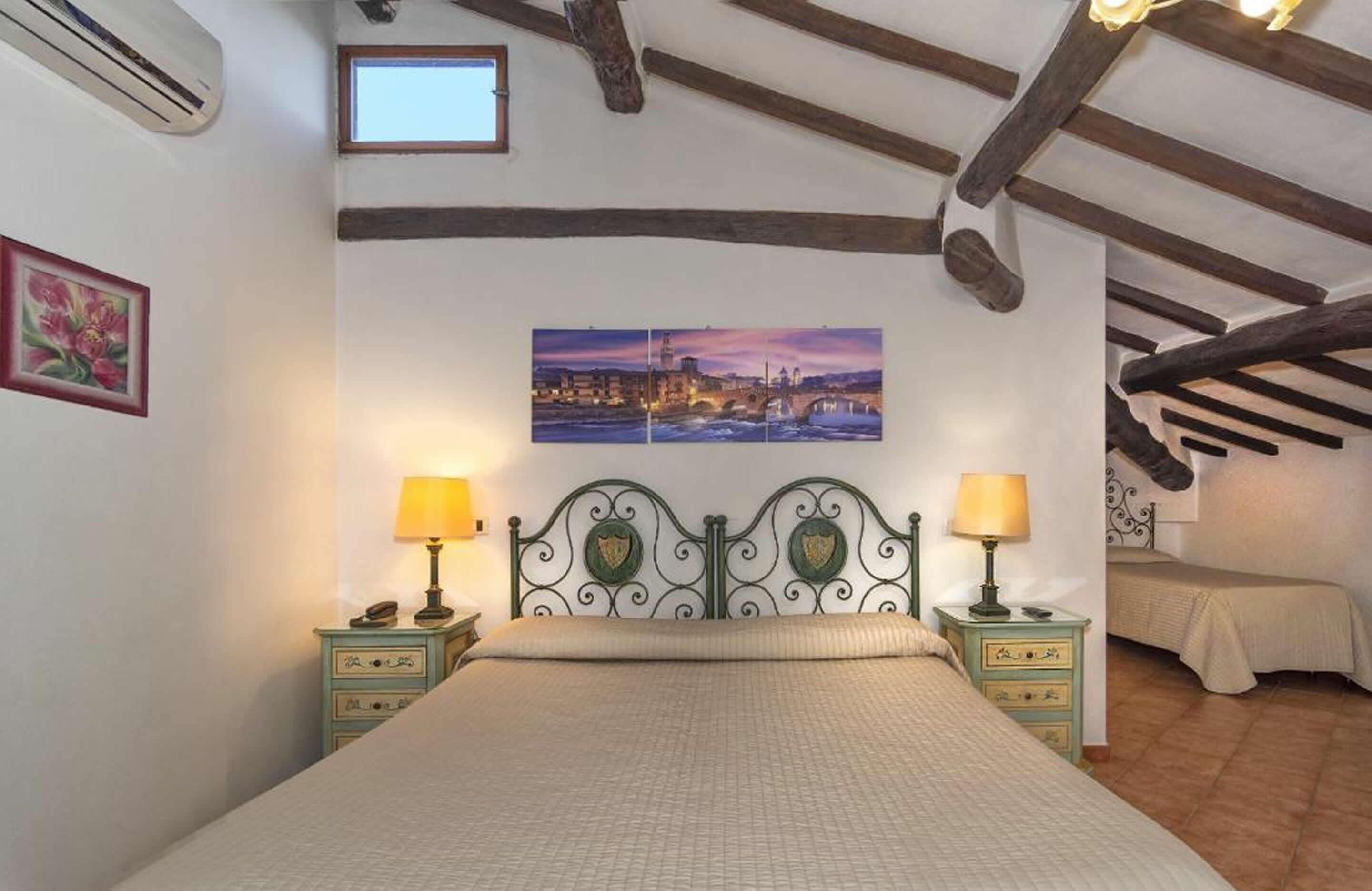 A bedroom with a bed, two bedside tables with lamps, a painting on the wall, and a window.
