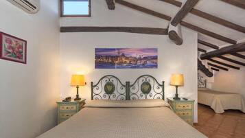 A bedroom with a bed, two bedside tables with lamps, a painting on the wall, and a window.