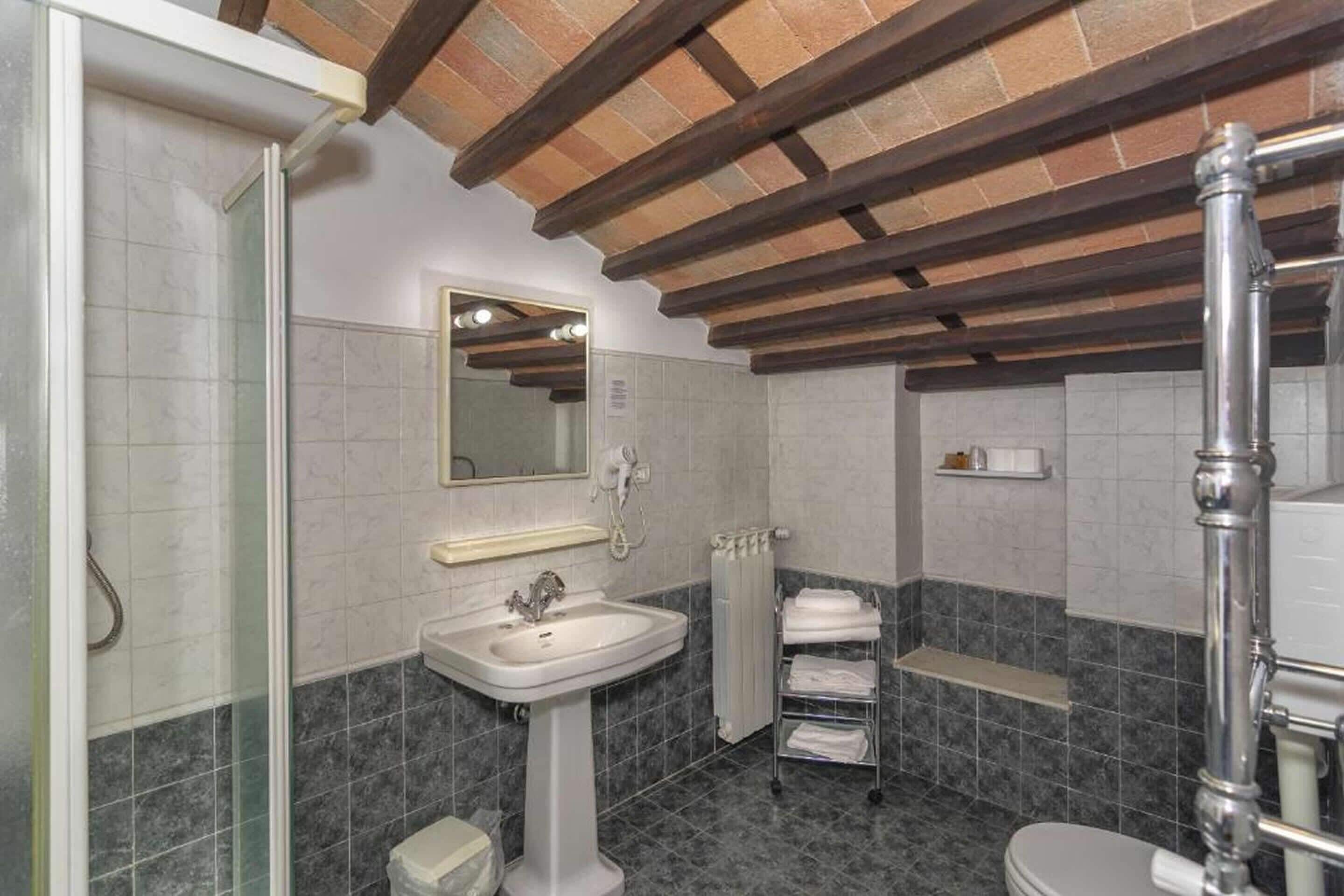 A bathroom with a pedestal sink, a mirror, a toilet, and a shower area.