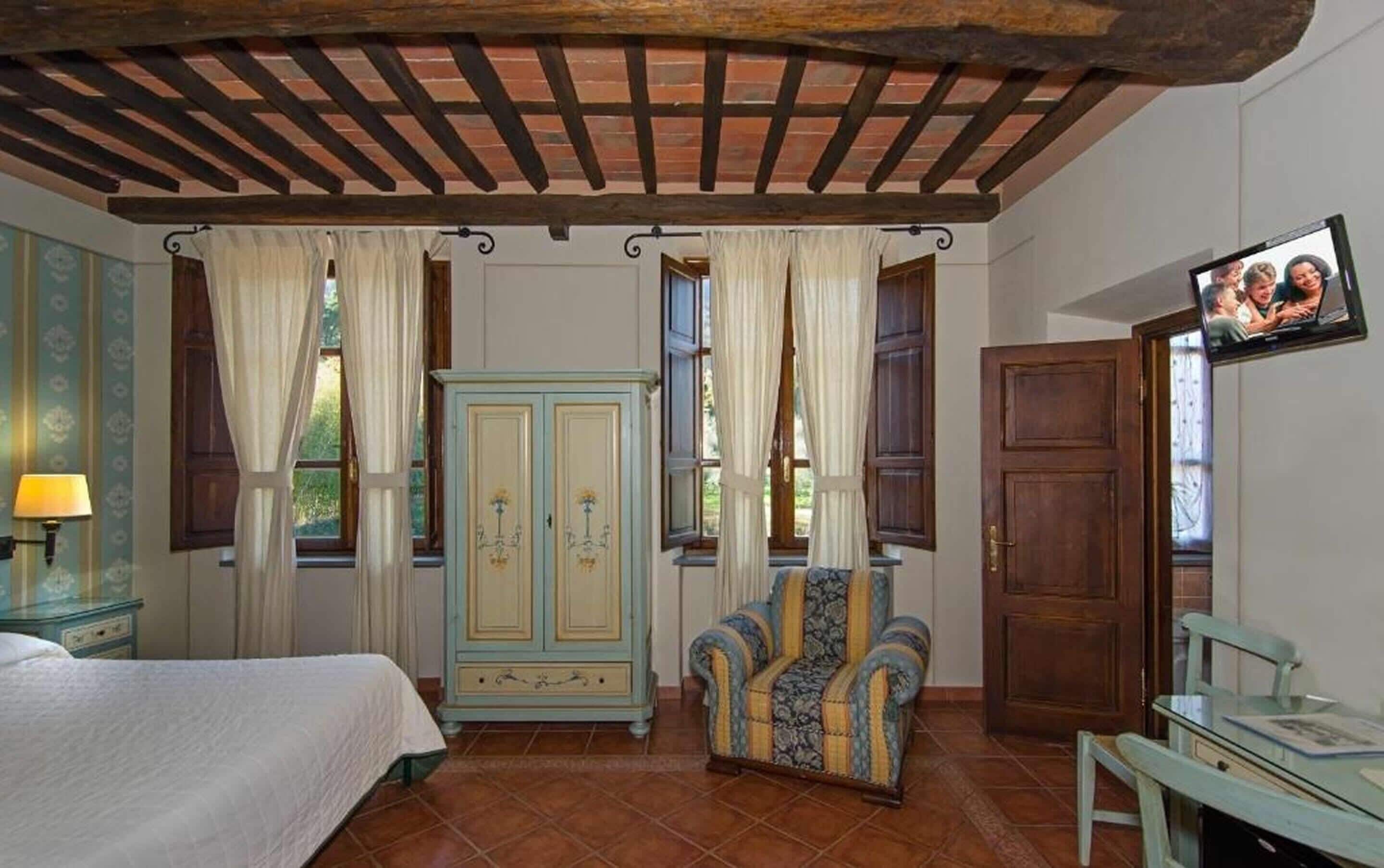 A room with a bed, a blue armchair, a wooden wardrobe, and a television on the wall.