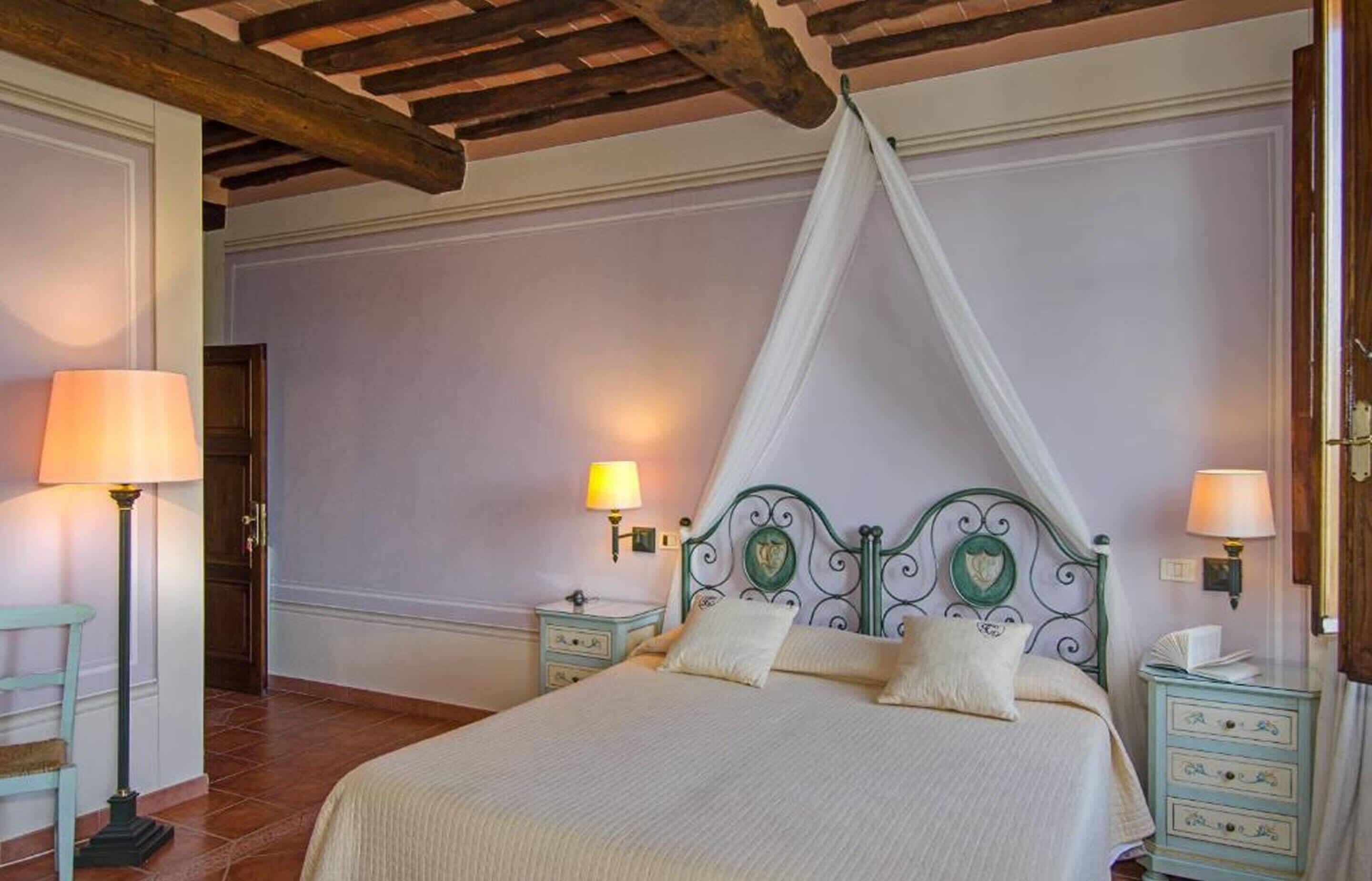 Un dormitorio con cama, dos mesitas de noche con lámparas, una silla y una viga de techo de madera.