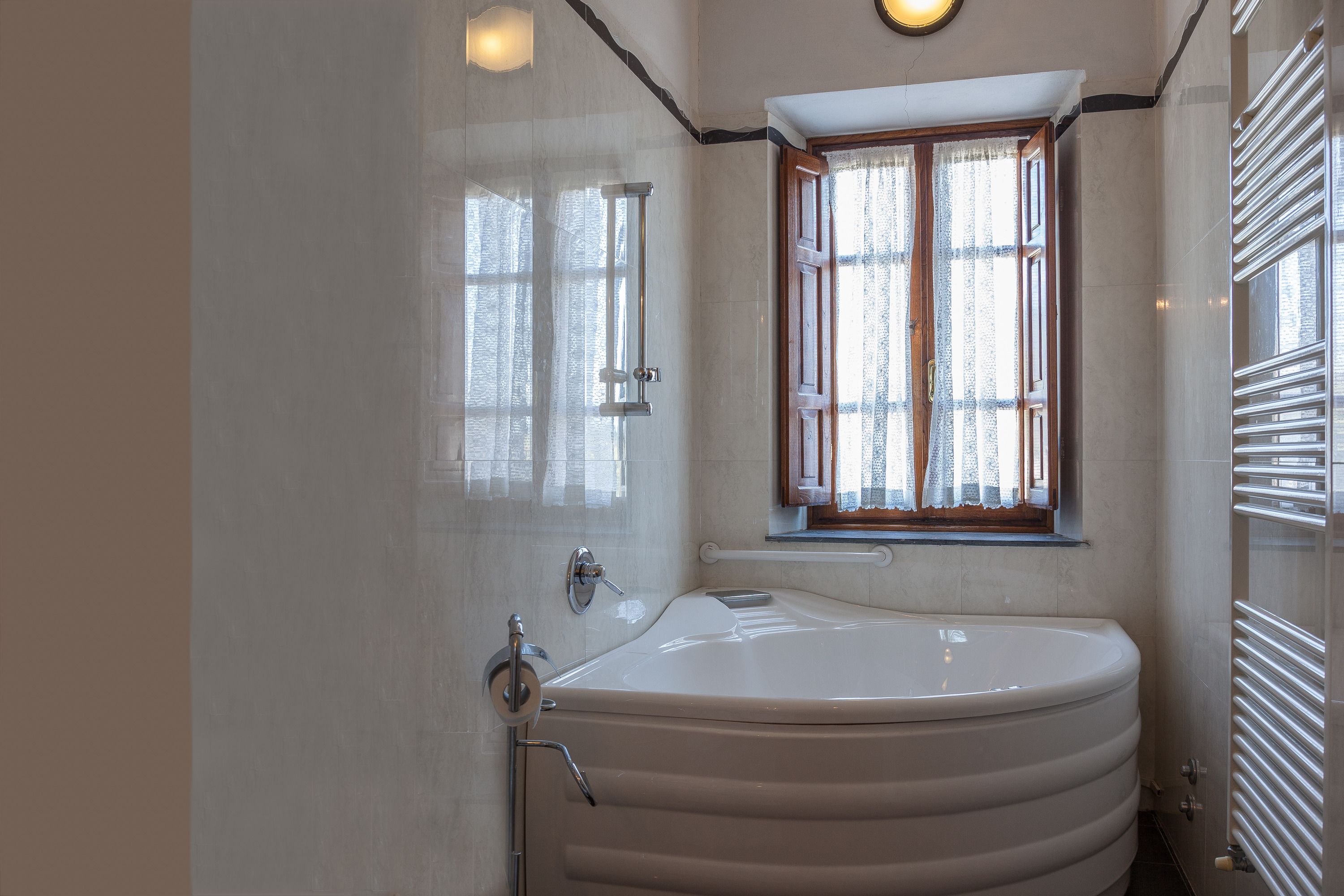 A modern bathroom with a freestanding bathtub, a window with curtains, and a towel rack.