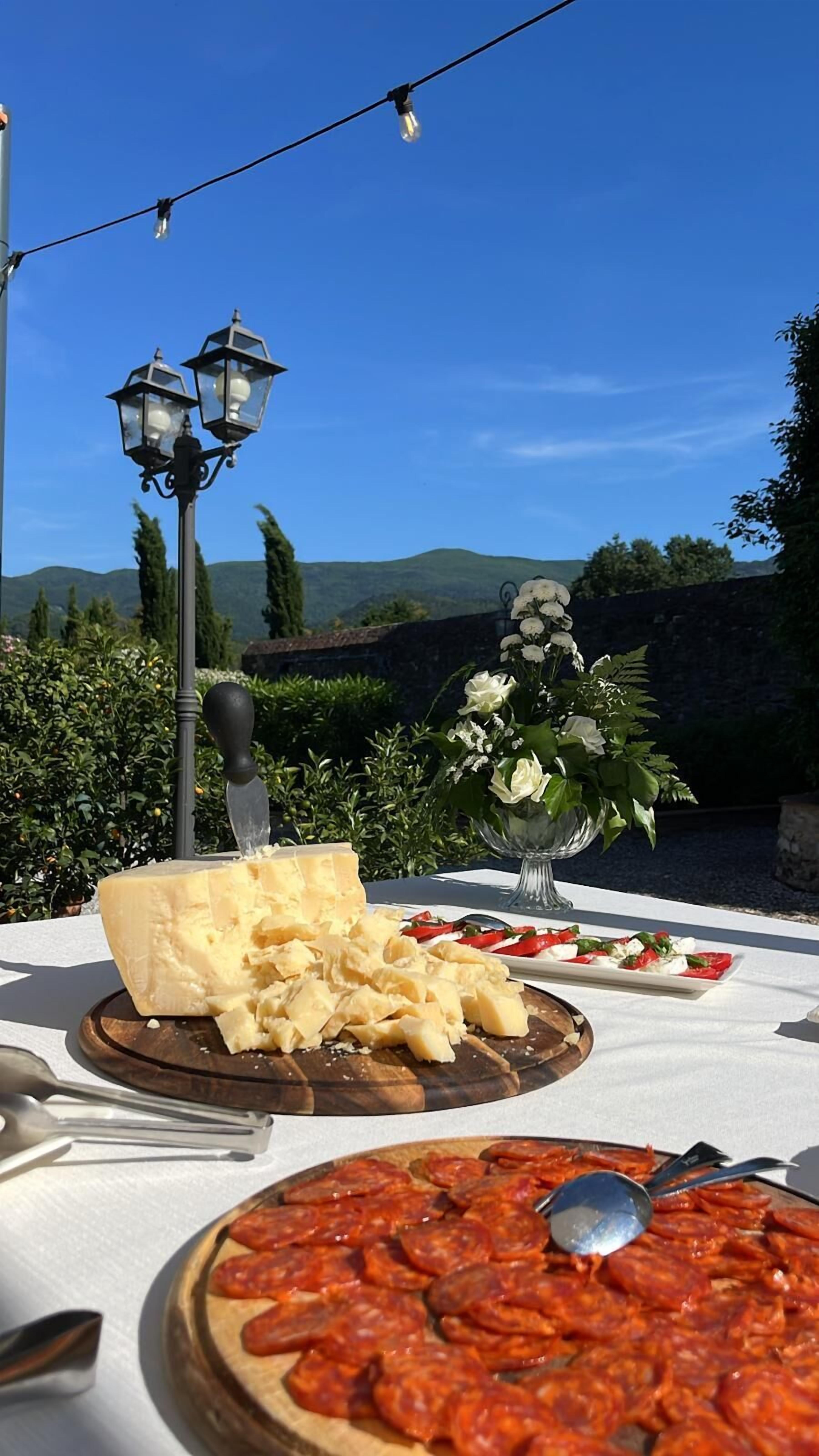 Montaje para comedor al aire libre con una tabla de quesos, un plato de embutidos y un arreglo floral.