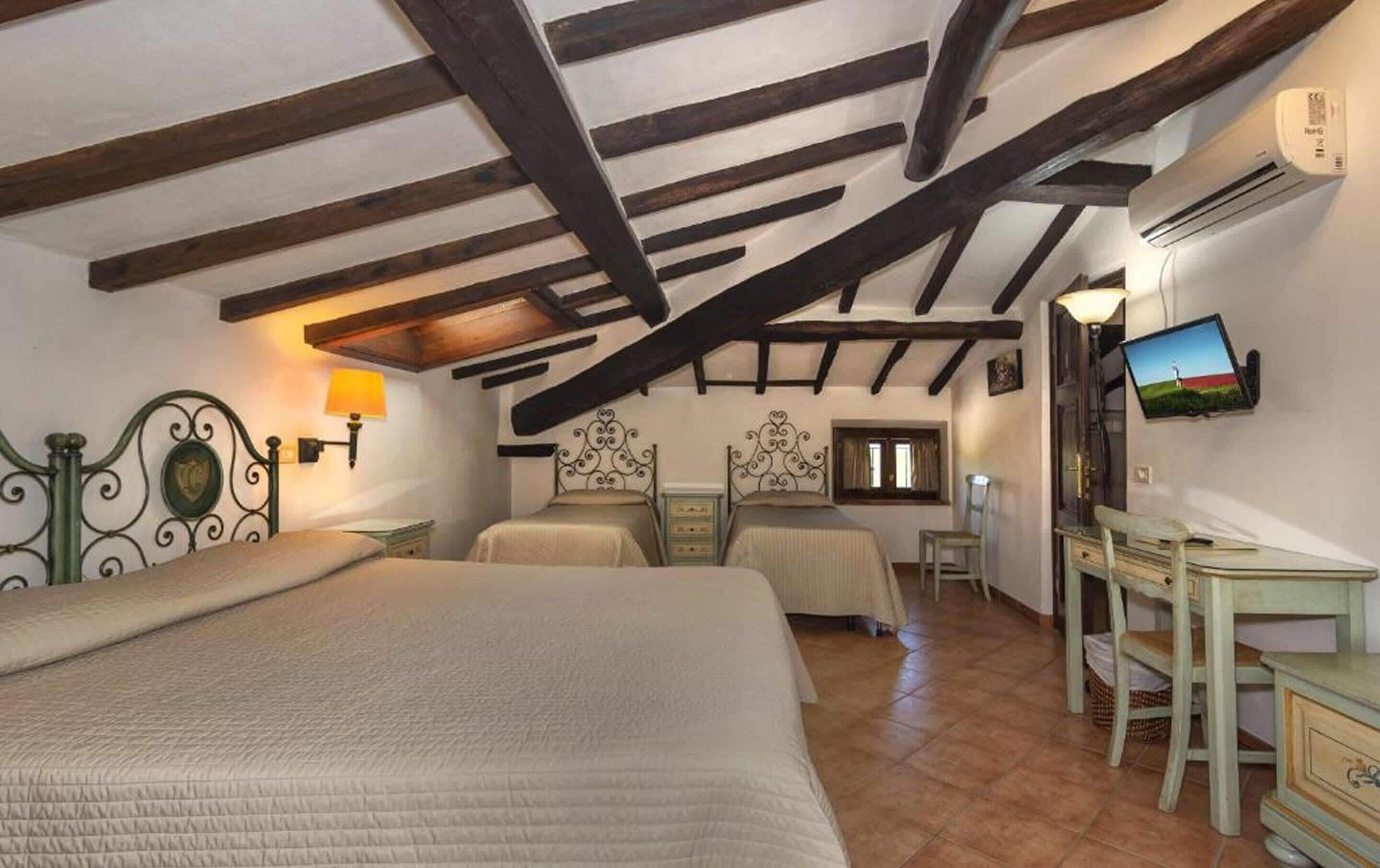 A bedroom with two beds, a desk, a television, and a window.