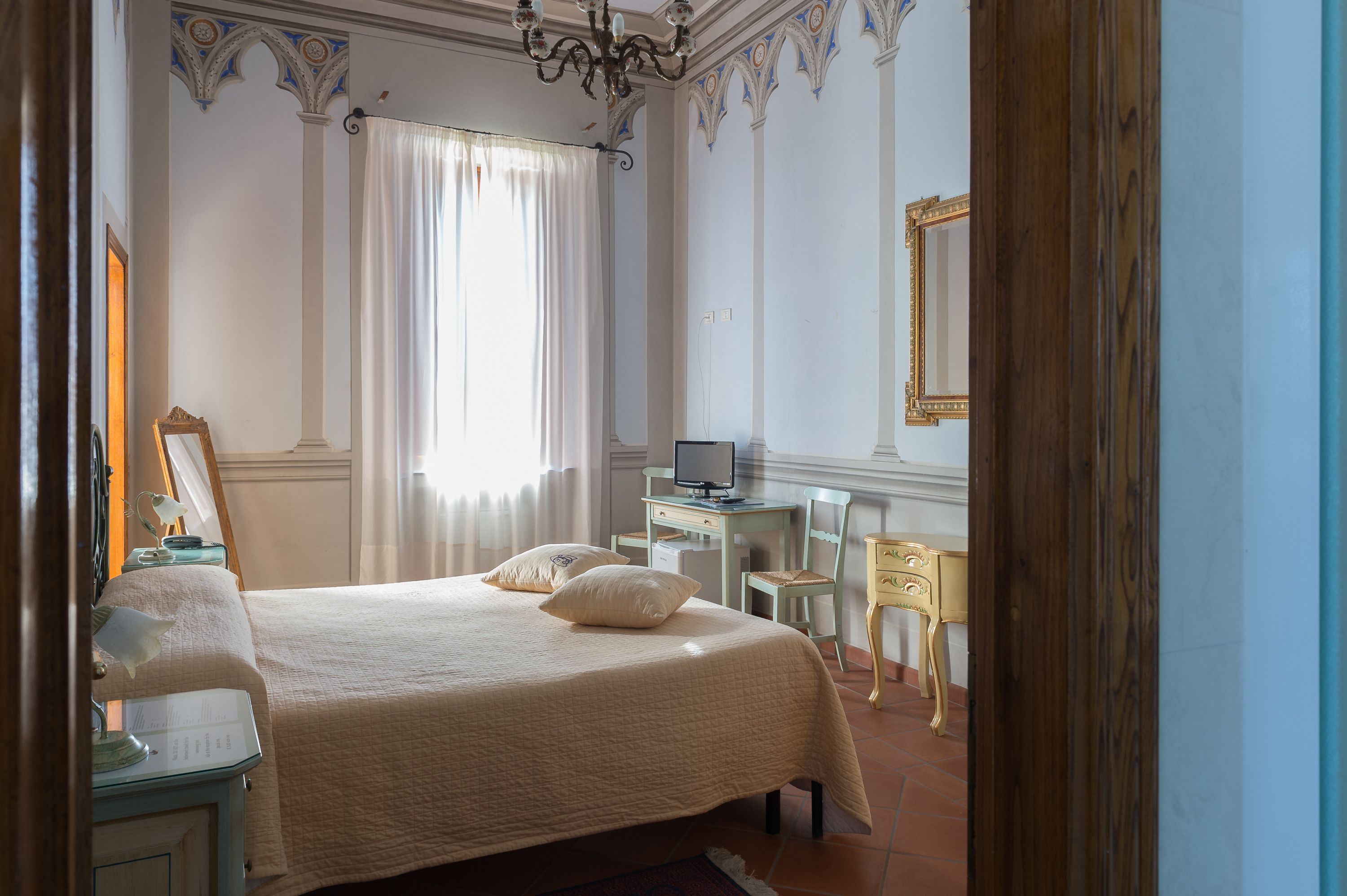 A bedroom with a bed, a desk, a chair, a television, and a mirror.