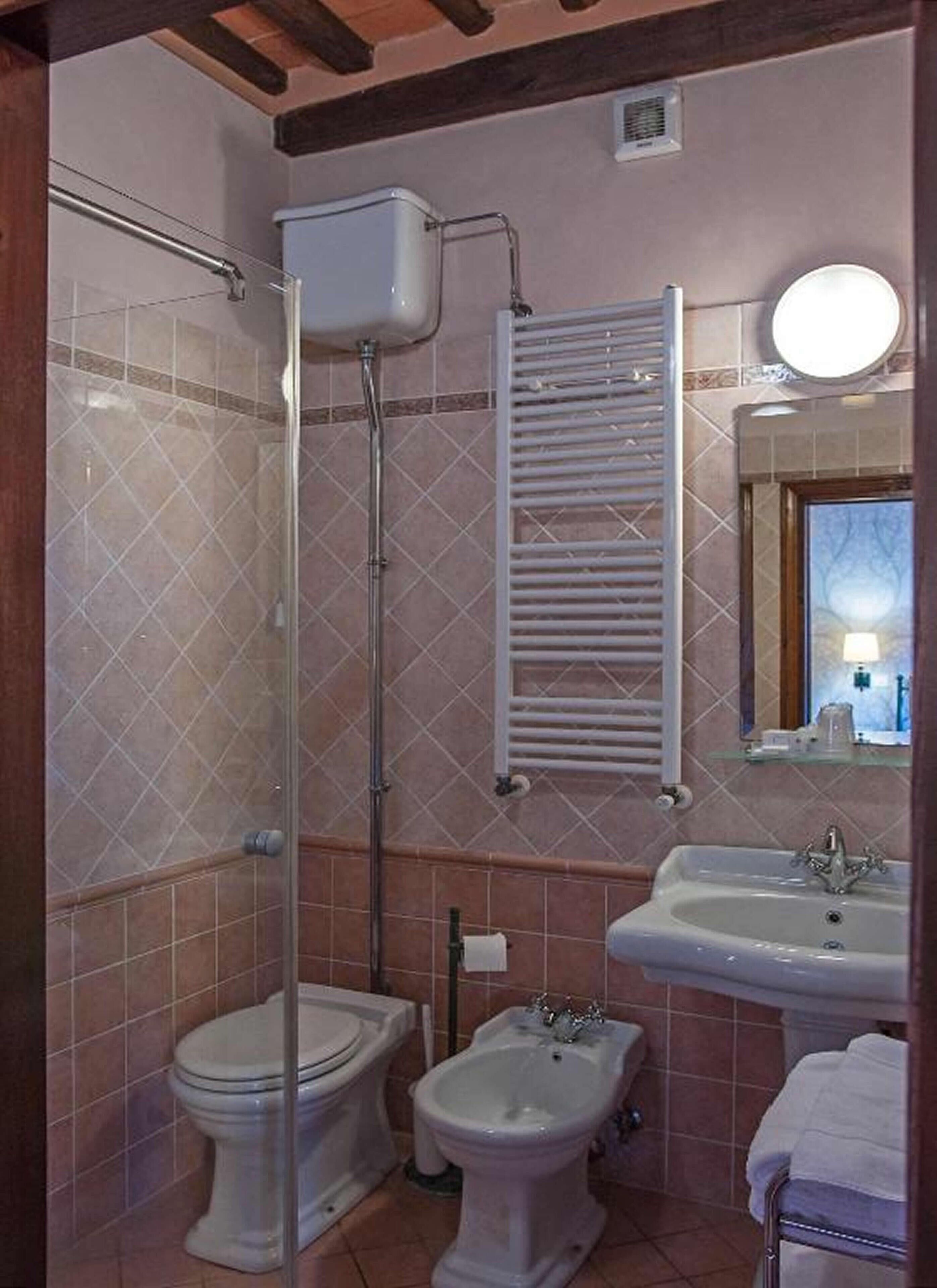 Un baño con inodoro, bidé y lavamanos, paredes con azulejos y un perchero para toallas.