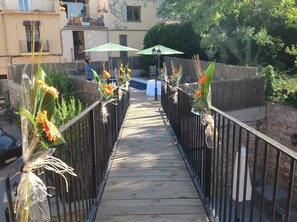 A wooden bridge with flower arrangements on both sides, leading to a building with a balcony. - Hostal Can Missè (Collbato)