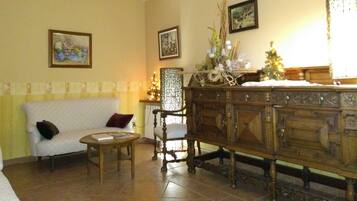 Uma sala de estar com um sofá branco, uma cadeira de madeira, um armário de madeira e uma mesinha. Há duas fotos emolduradas na parede.