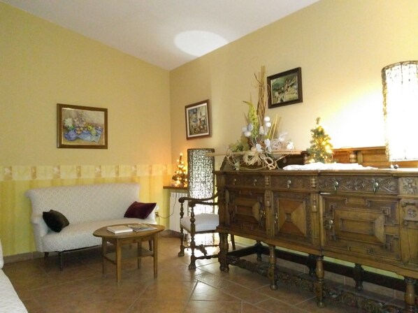 A living room with a white sofa, a wooden chair, a wooden cabinet, and a small table. There are two framed pictures on the wall. - Hostal Can Missè (Collbato)