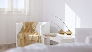 Una habitación minimalista con un sofá blanco, un plaid dorado y dos jarrones dorados sobre una mesita blanca.