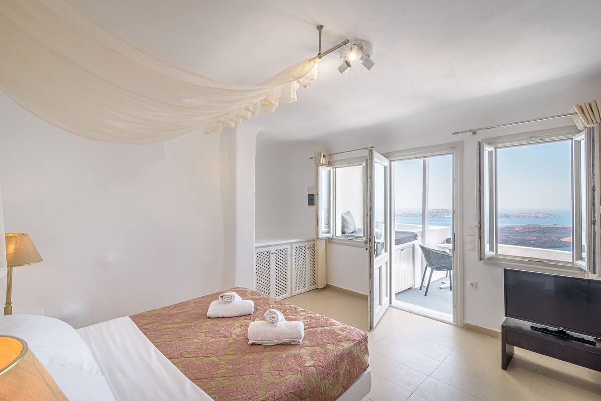 A hotel room with a bed, a TV, a balcony with a view, and a ceiling fan.