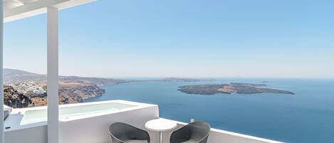 A balcony with two chairs and a small table overlooking a coastal view.