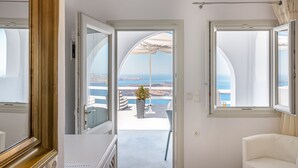 Habitación de hotel con vista al mar, un balcón con una silla blanca y un espejo grande.