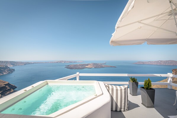A balcony with a hot tub overlooking a scenic view of the sea and islands. - Avianto Suites (Santorini)