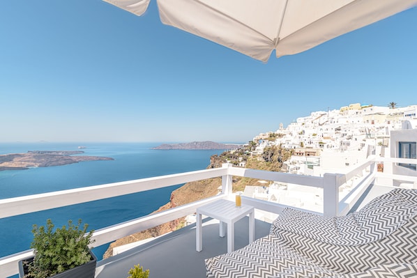 En balkon med hvid gelænder, udsigt over kysten med bygninger og havet.