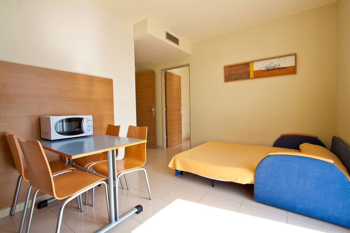 Ein Hotelzimmer mit Bett, Schreibtisch mit Stuhl, einer Mikrowelle und einer Tür zu einem anderen Raum.