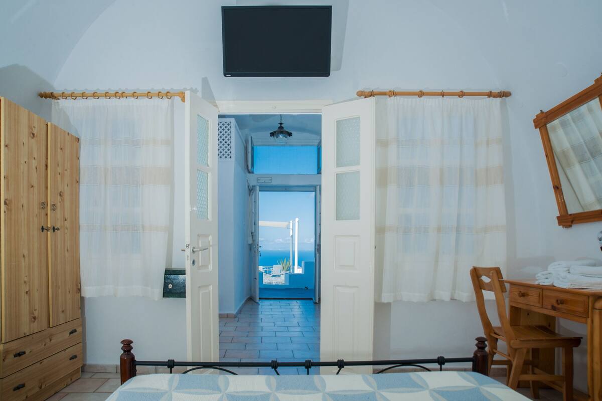 Un dormitorio con cama, armario de madera, escritorio con silla y vistas a un balcón por una puerta abierta.