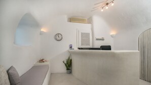Una habitación minimalista con un mostrador de recepción curvo, un reloj, una planta pequeña y un sofá.