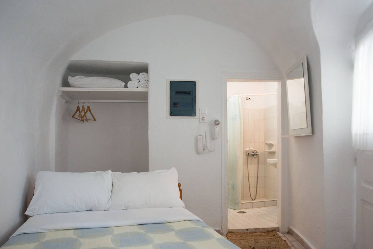 Un dormitorio con cama, perchero, estante con toallas, teléfono y zona de ducha.