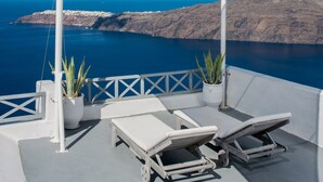 Una terraza con dos tumbonas y un dosel blanco, con vistas a un paisaje costero y un cielo azul despejado.