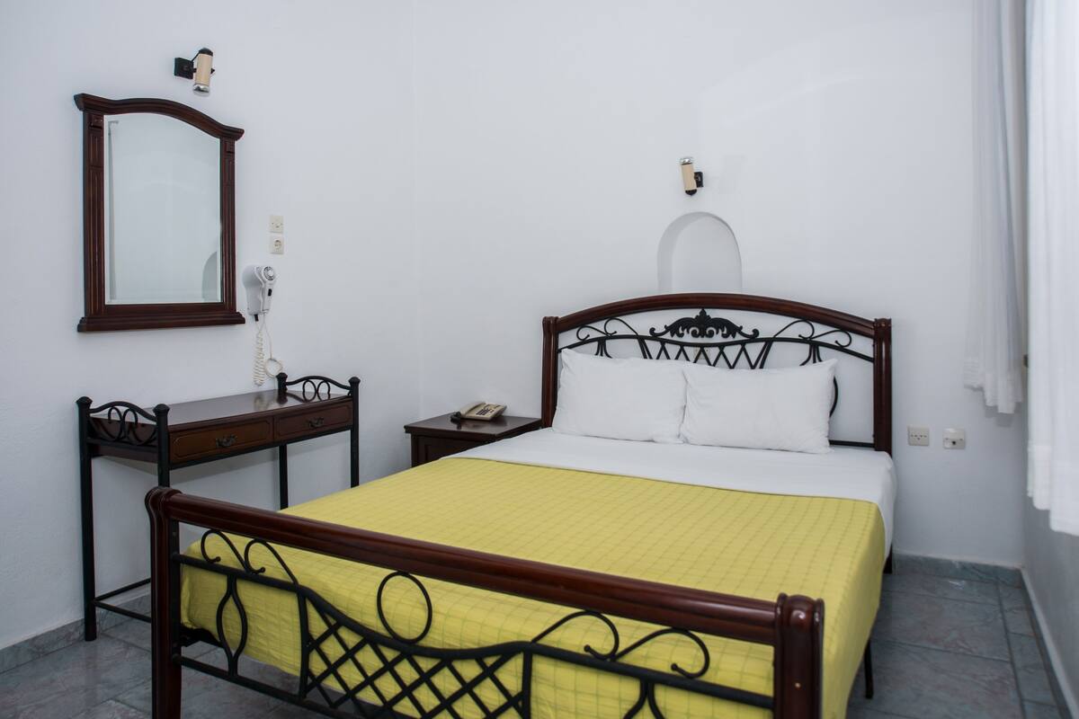Un dormitorio ordenado con cama, mesita de noche y un espejo en la pared.