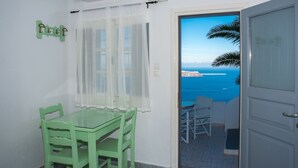 Una habitación con una mesa y sillas de vidrio, una puerta que da a un balcón con vistas al mar y acantilados.