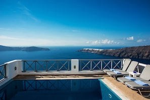 Zona de piscina con sillones de descanso y vista al mar y las montañas.