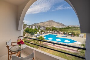 Un balcón con vista a una piscina, sillas de descanso y una montaña al fondo.