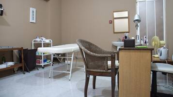 Professional workspace with a white examination table, wicker chair, and desk.