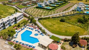 Et resort med en stor swimmingpool, flere bygninger og udsigt til havet og bakker.