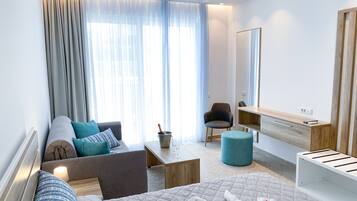 Una habitación de hotel moderna con sofá, sillón, mesita de noche y cama con cubrecama acolchado.