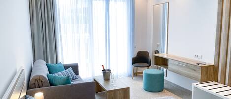 Una habitación de hotel moderna con sofá, sillón, mesita de noche y cama con cubrecama acolchado.