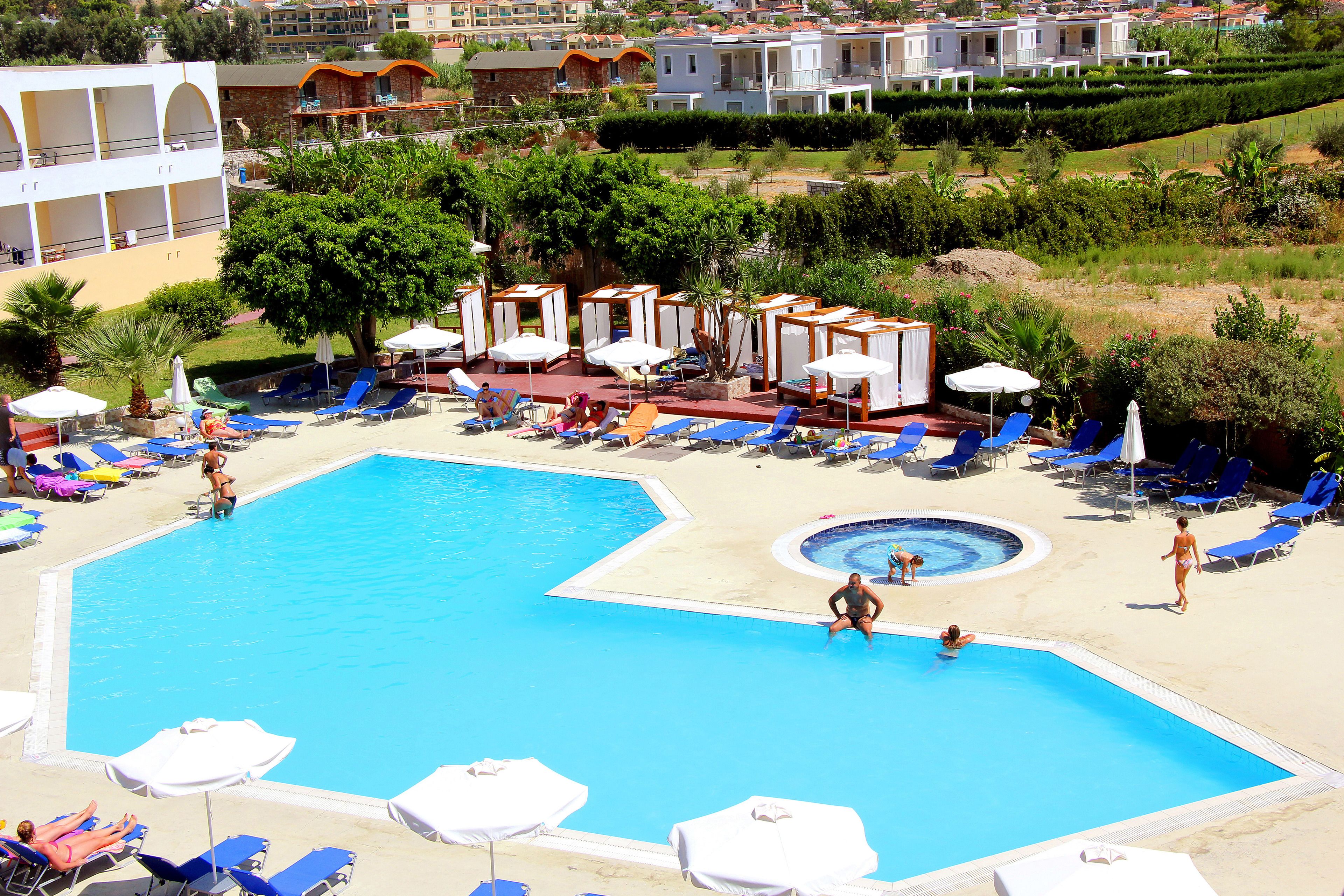 Ein großer Pool mit Liegestühlen und Sonnenschirmen, umgeben von Grünflächen und Gebäuden.