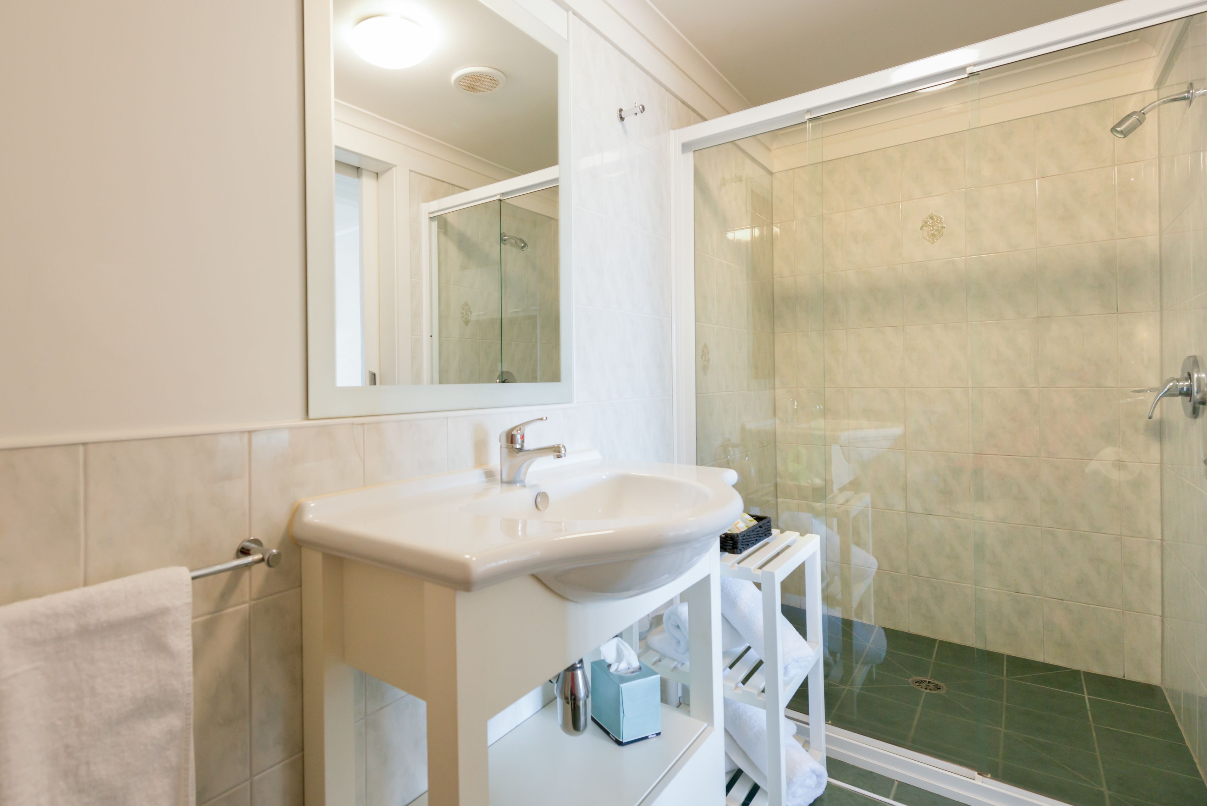 Un baño con lavamanos blanco, espejo y cabina de ducha con puertas de vidrio.