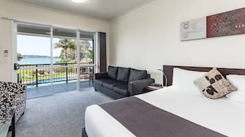 Een hotelkamer met een groot bed, een bank, een tafel en een balkon met uitzicht op een zwembad.