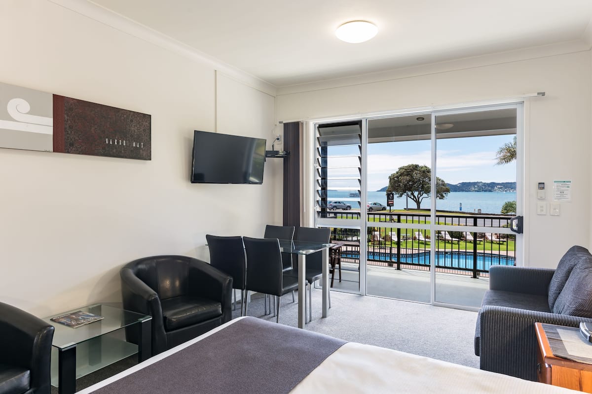 Habitación de hotel con cama, televisión, mesa de vidrio y sillas. Tiene un balcón con vistas a la piscina.