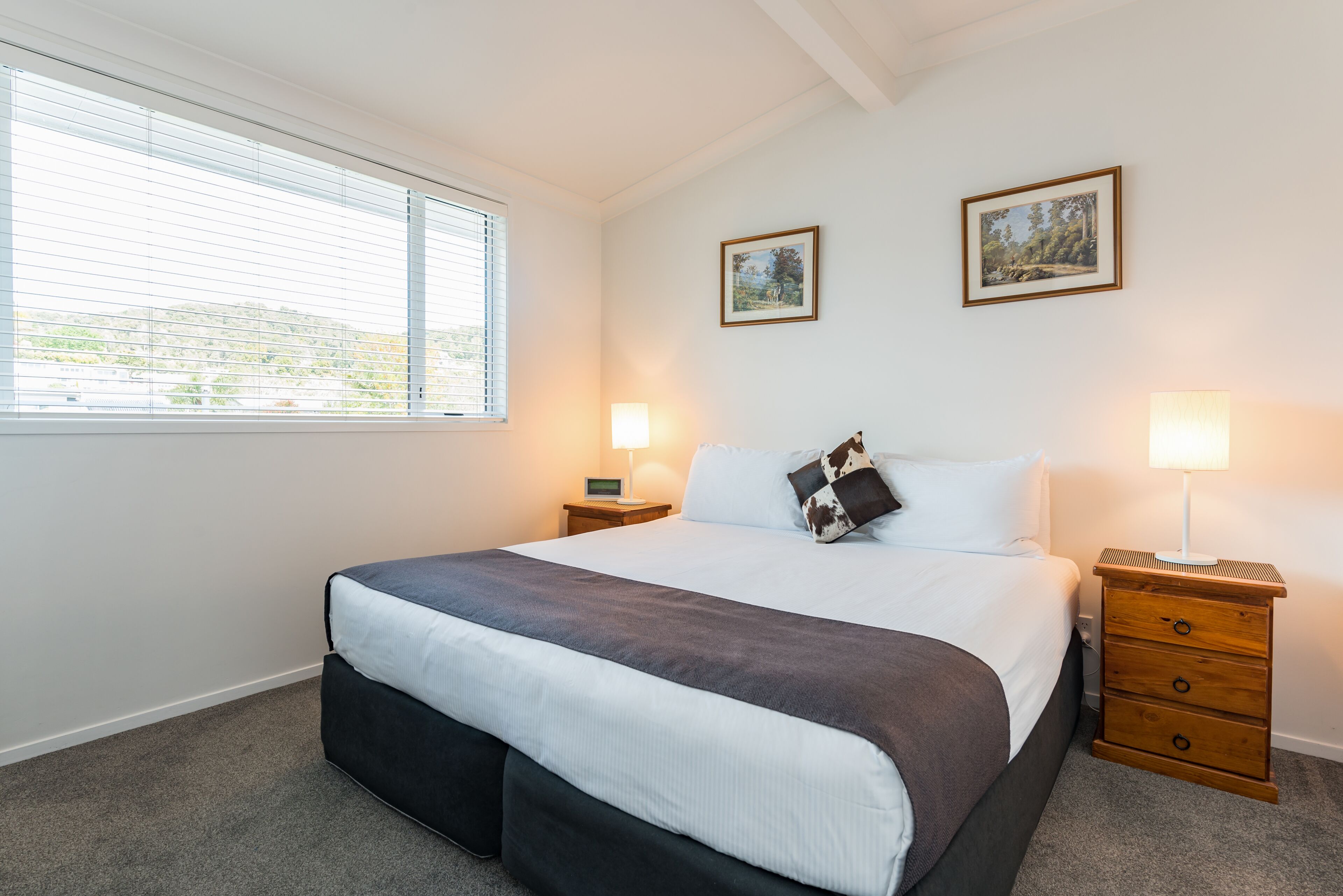 A neatly made bed with a dark and white duvet, two bedside tables with lamps, and two framed pictures on the wall.