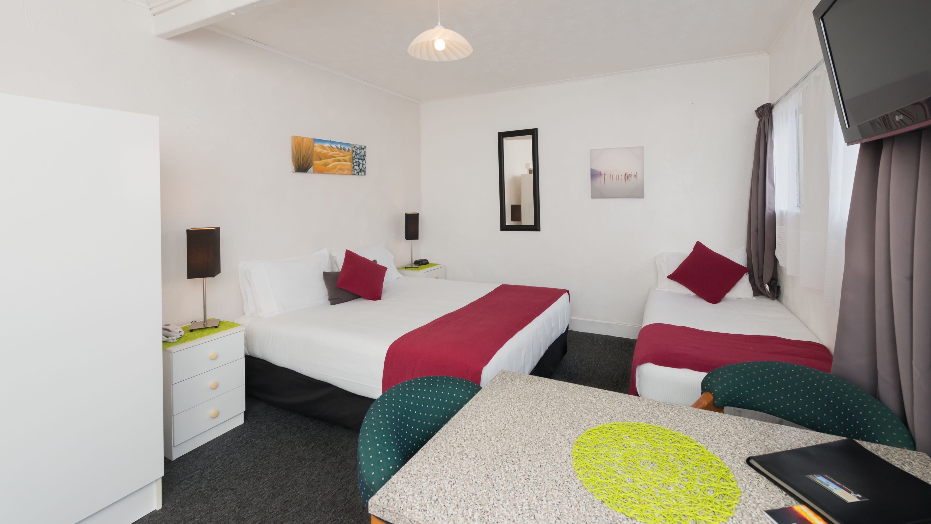 Habitación de hotel con dos camas, un escritorio y una silla. Hay un cuadro en la pared, un espejo y un televisor montado.