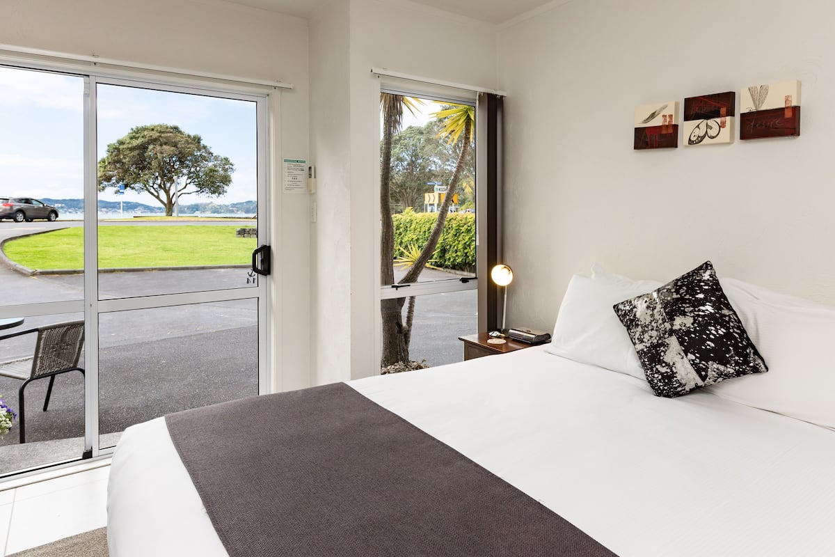 Habitación de hotel con cama, mesita de noche, lámpara y vistas al exterior a través de una puerta corrediza.