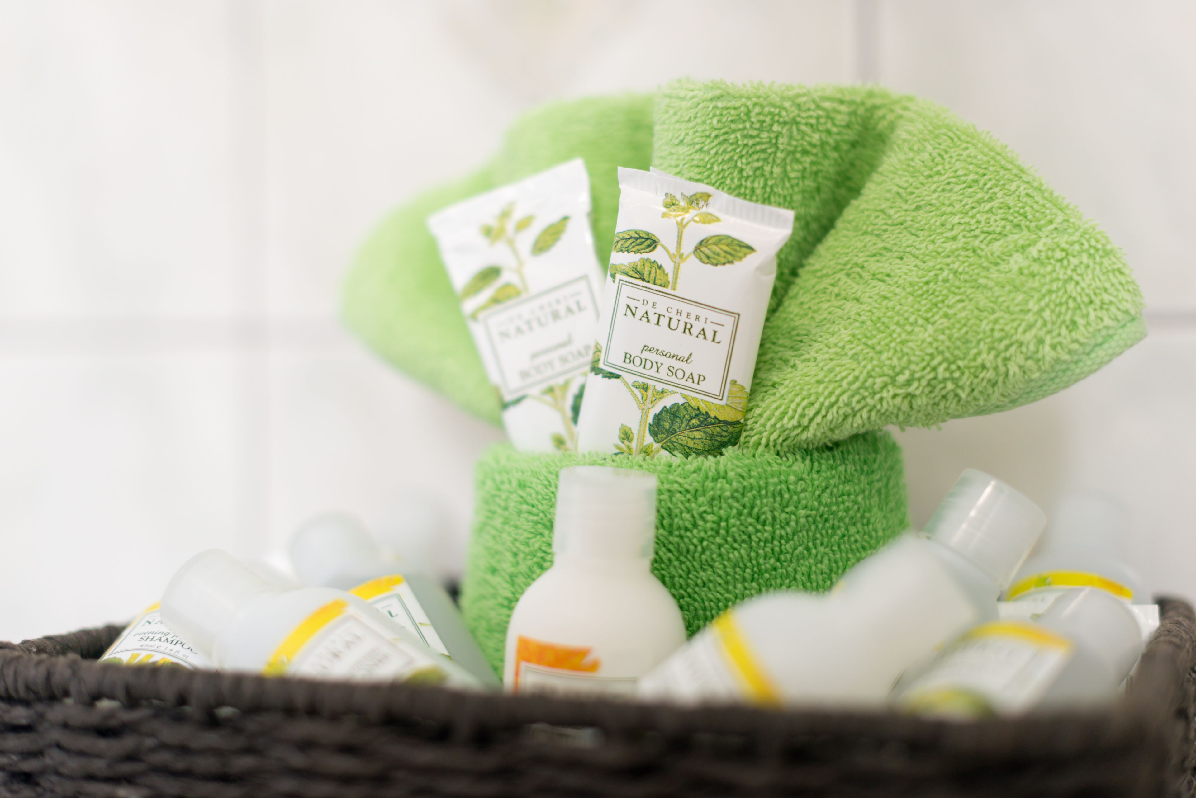 A basket containing green towels and bottles of De Cheri Natural personal body soap.