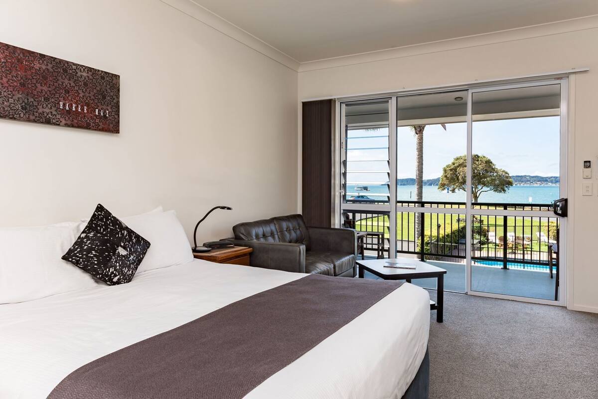 Habitación de hotel con cama, una silla, una mesa y un balcón con vista al mar.