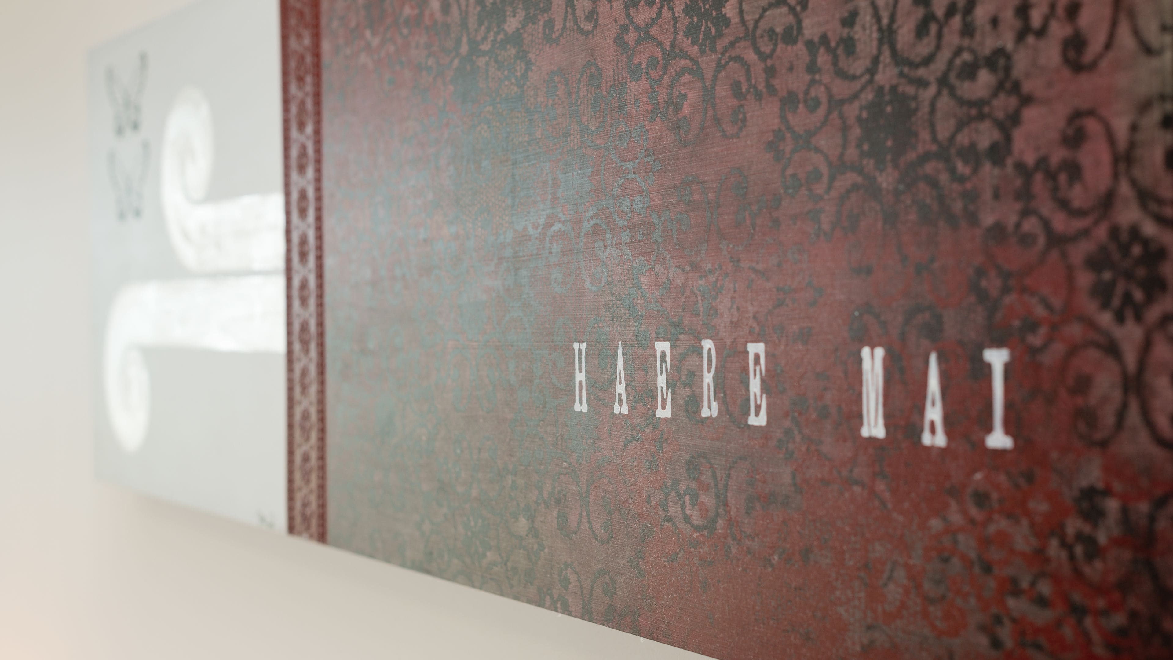 A wall with a decorative pattern and the text "HAERE MAI" in white letters.