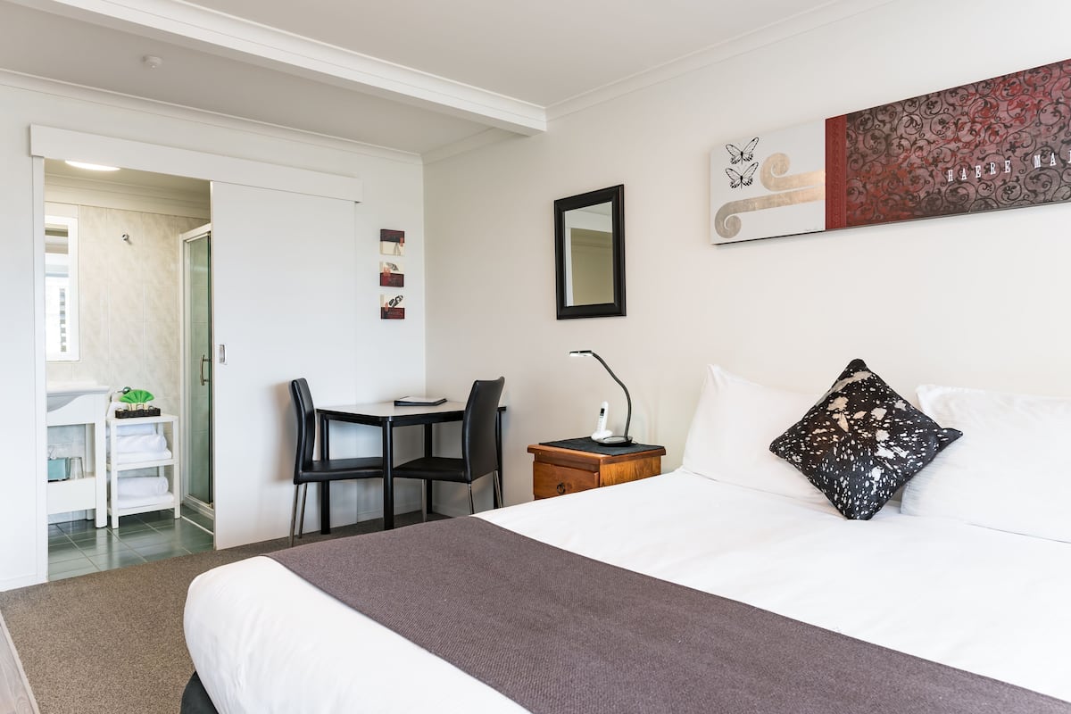 Una habitación de hotel con cama, escritorio, silla, mesita de noche y espejo.