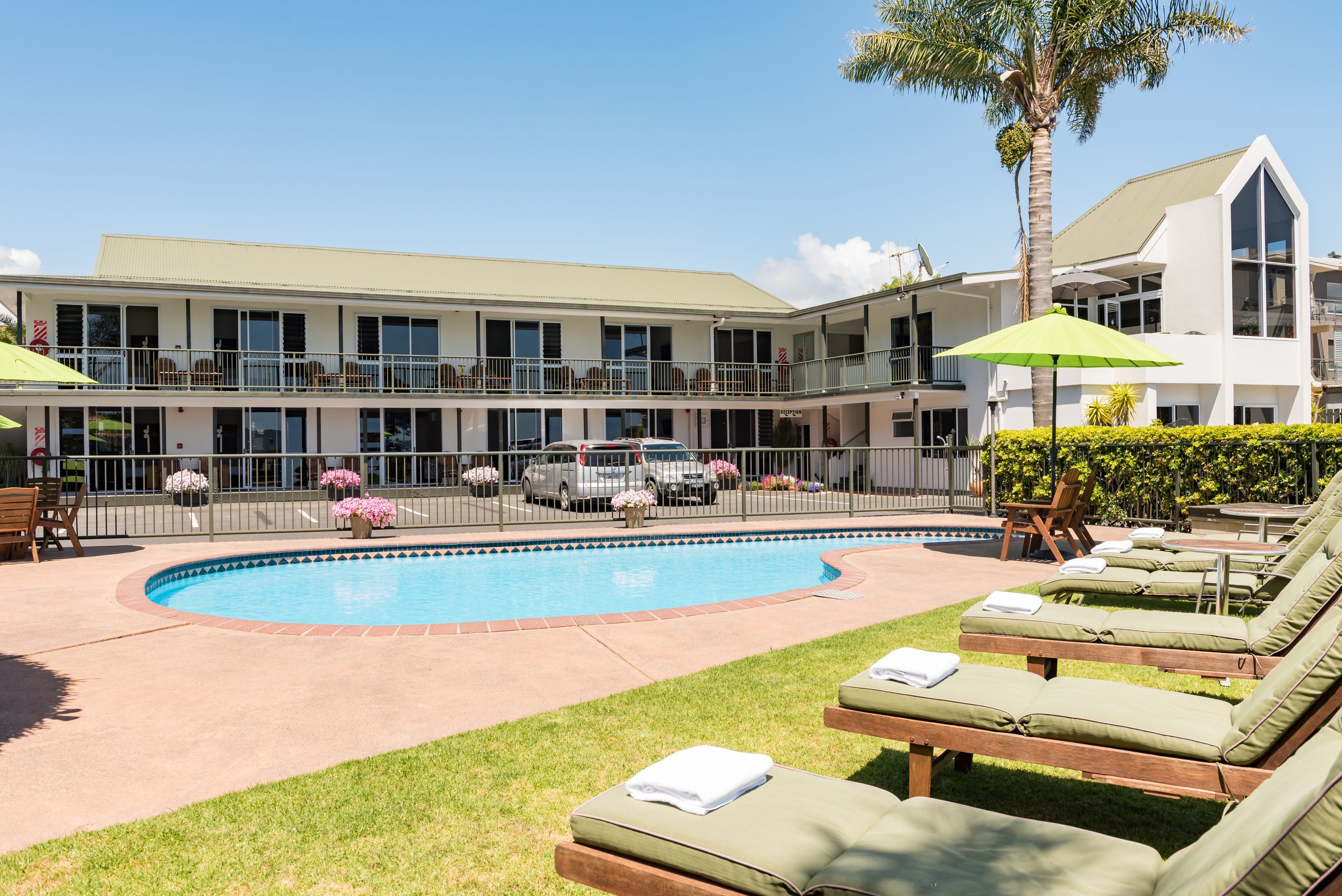 A hotel with a swimming pool, lounge chairs, and a two-story building with balconies.