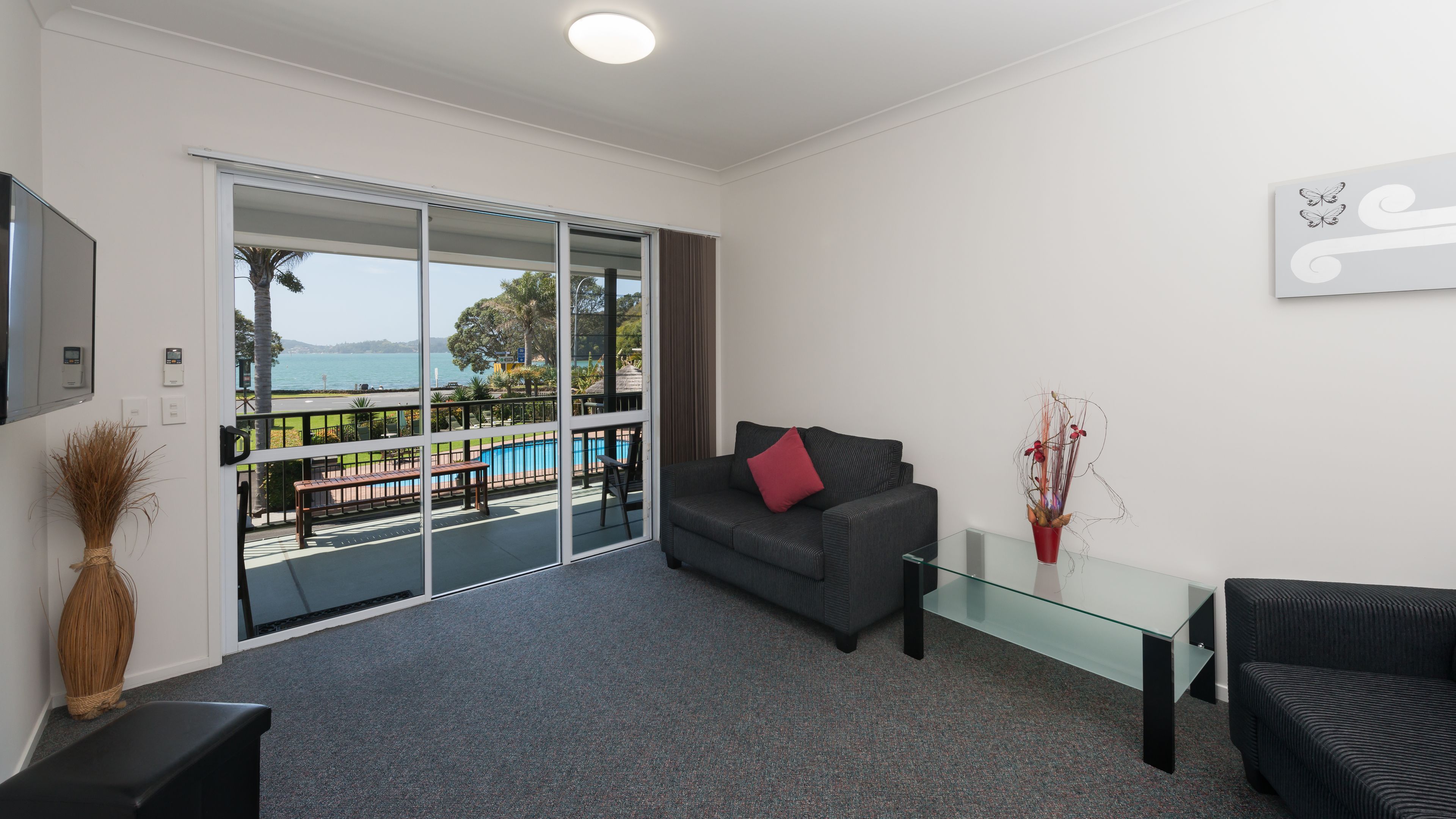 A modern living room with a grey sofa, a glass coffee table, and a view of a pool and outdoor area.