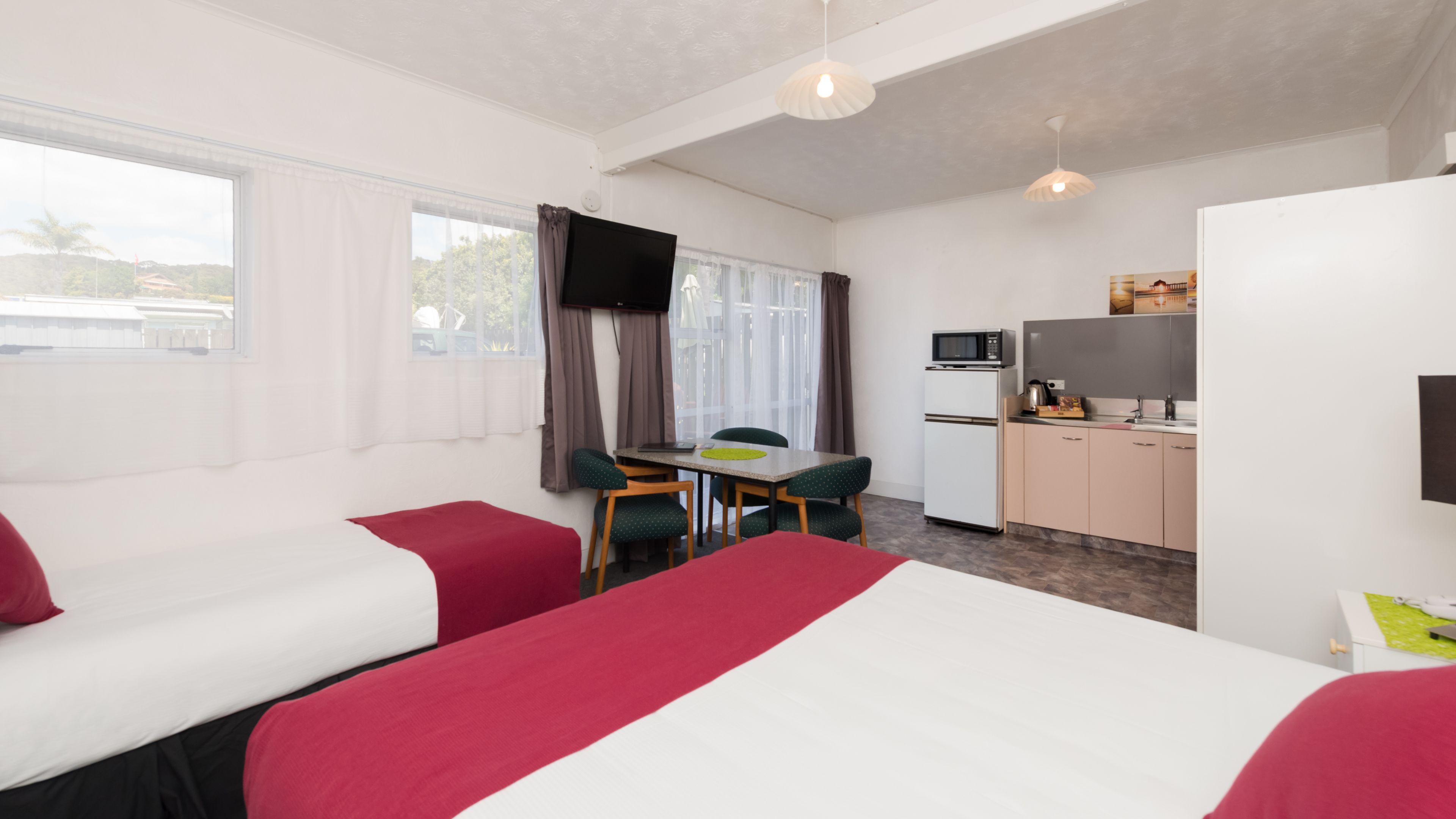 A hotel room with two beds, a small kitchenette, a dining table with chairs, and a TV.