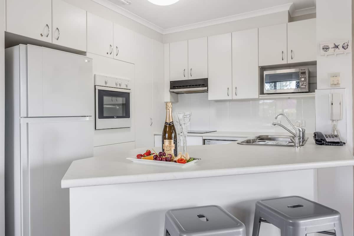 A modern kitchen with white cabinets, a built-in oven, a microwave, and a bar area with stools.