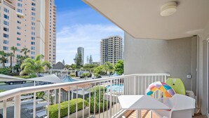 Un balcón con vista a la piscina, muebles de exterior blancos y un balón de playa colorido.