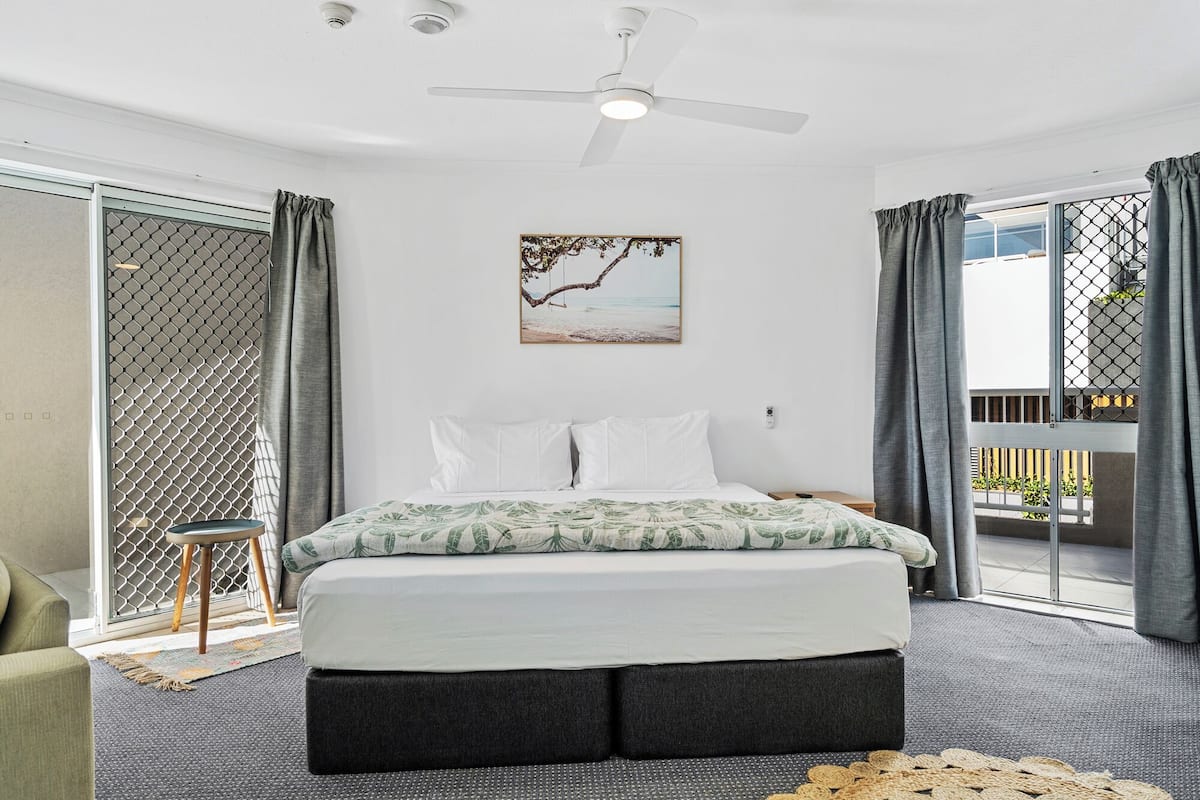 A modern bedroom with a bed, a ceiling fan, and a view of the outside through a sliding glass door.